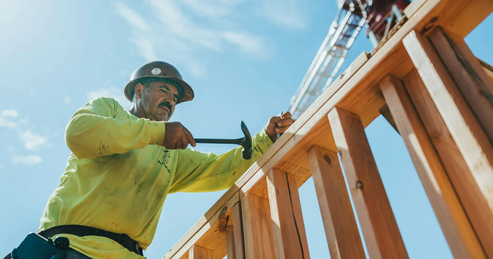 A construction worker in a hard hat hammering a wooden wall frame on site